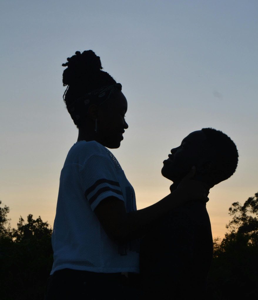 Side view of young African American couple hugging each other and enjoying time together against cloudless sundown sky in evening